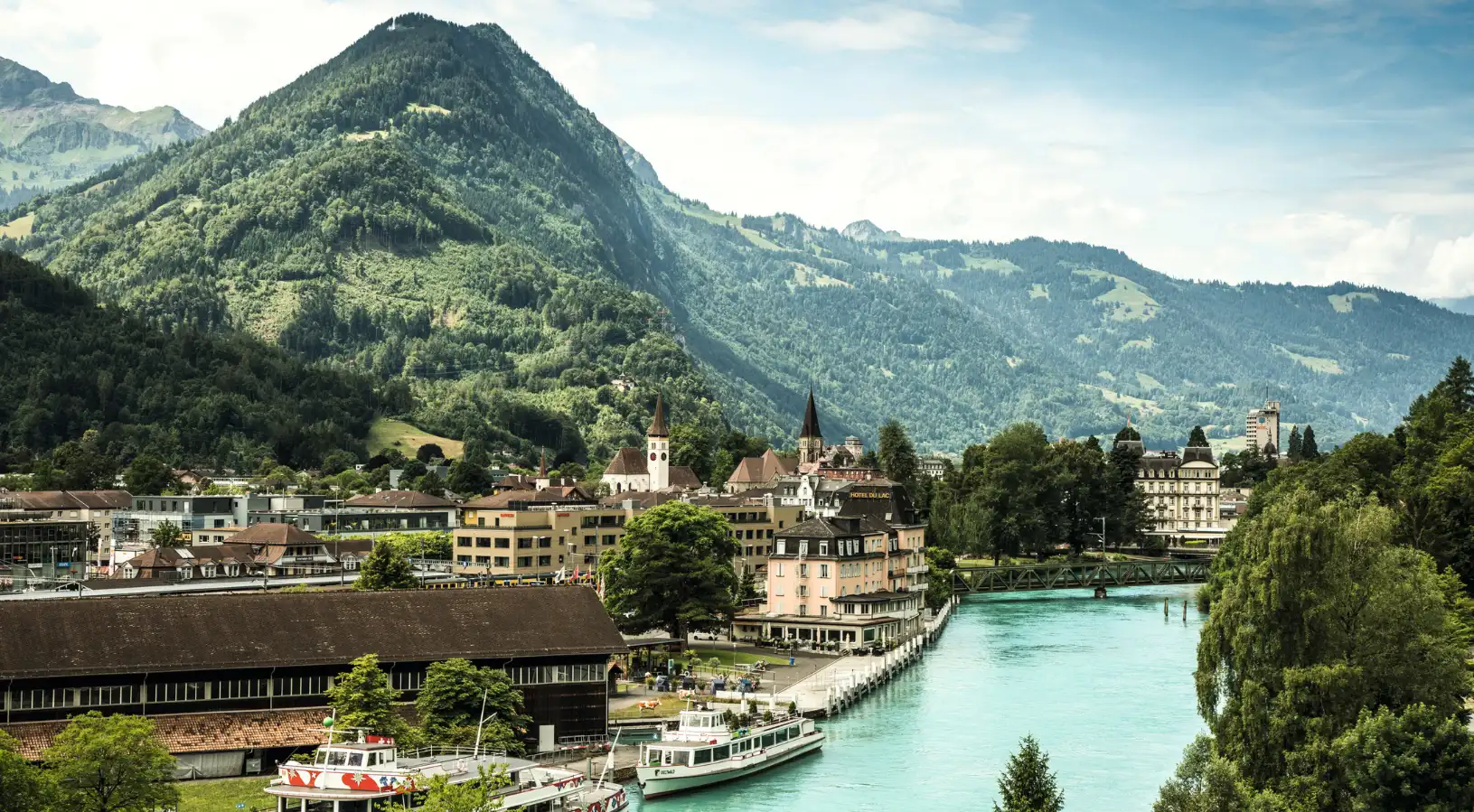 A sweeping view of the town of Interlaken and the turquoise Aare River with mountains in the background, illustrating the central hub for things to do in Interlaken.