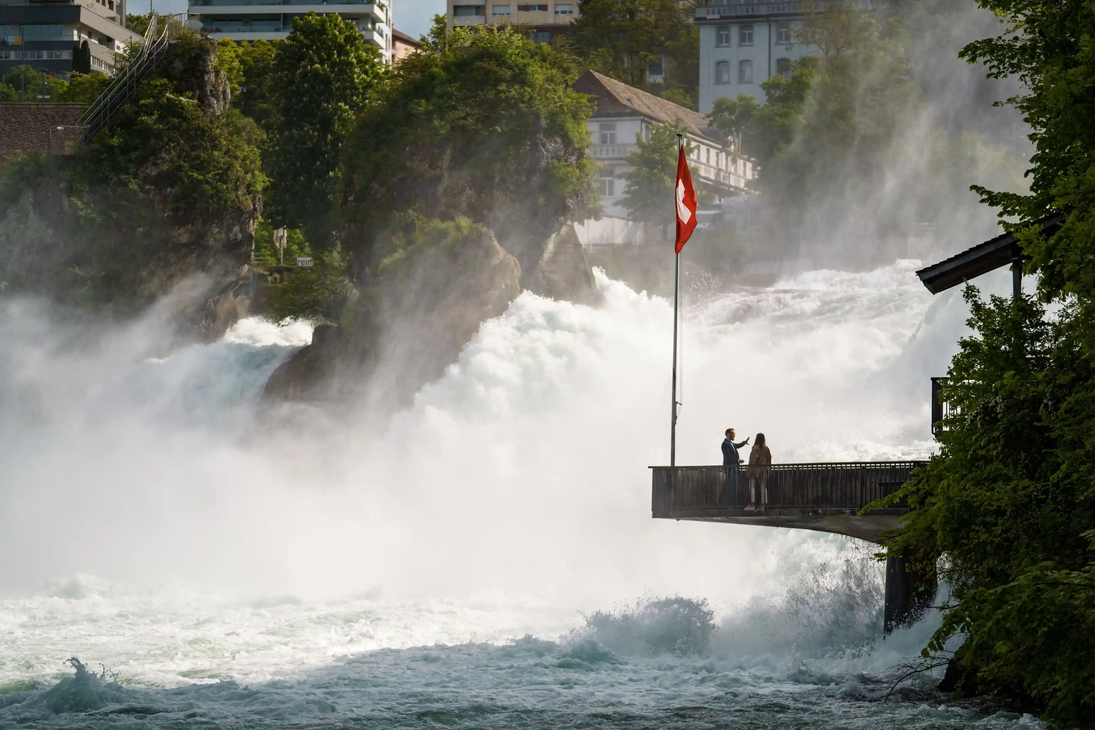 Two People admiring the majestic Rhine Falls, it can be easily considered as one of the Hidden Gems with Swiss Travel Pass