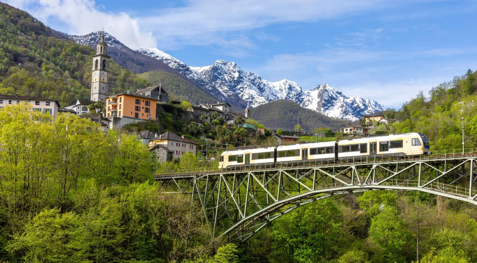 Swiss train passing a mountain village and a steel bridge, showing local routes included in How the Swiss Travel Pass Works on Trains.