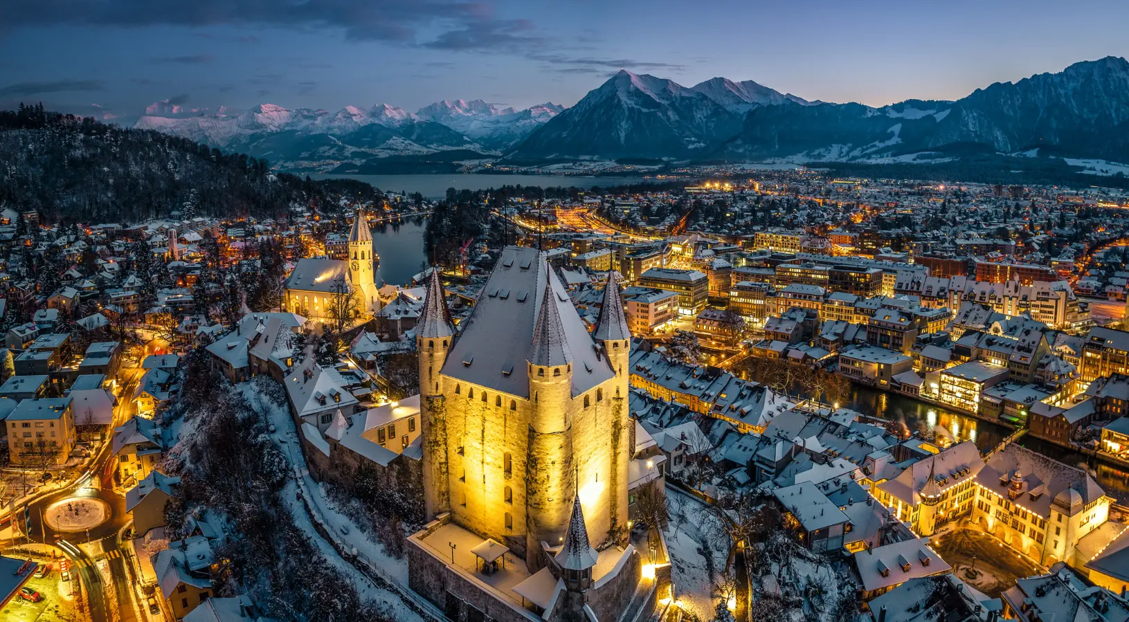 A cozy Swiss village in winter, covered in deep snow beneath towering alpine peaks, with skiers in the distance, highlighting that the best time to visit Switzerland is for snowy adventures in winter.