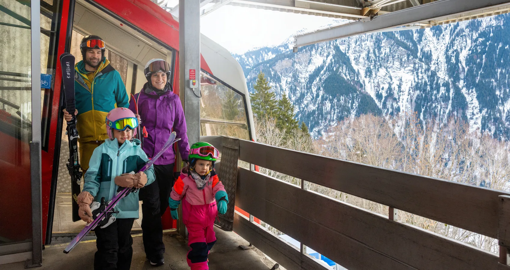 Family with two young children carrying skis as they step off the cable car at Braunwald mountain station
