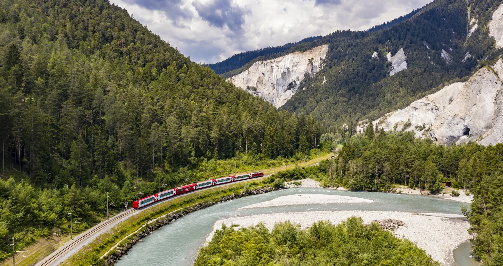 Red Glacier Express train curving along the turquoise river through the forested Rhine Gorge in Switzerland