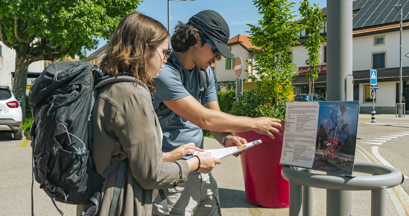Two backpackers reading a trail information board in Le Noirmont, Doubs Natural Park, Switzerland