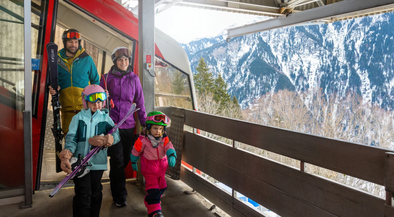 A family with two young children carrying skis stepping off a mountain train at Braunwald, illustrating free travel for children with the Swiss Travel Pass and Swiss Family Card