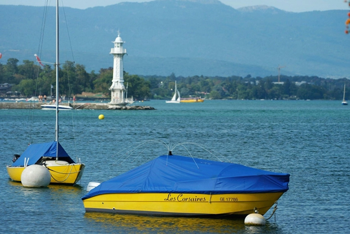 Colorful boats gently floating on the tranquil waters of Lake Geneva, surrounded by picturesque mountains and the vibrant cityscape of Geneva, Switzerland.